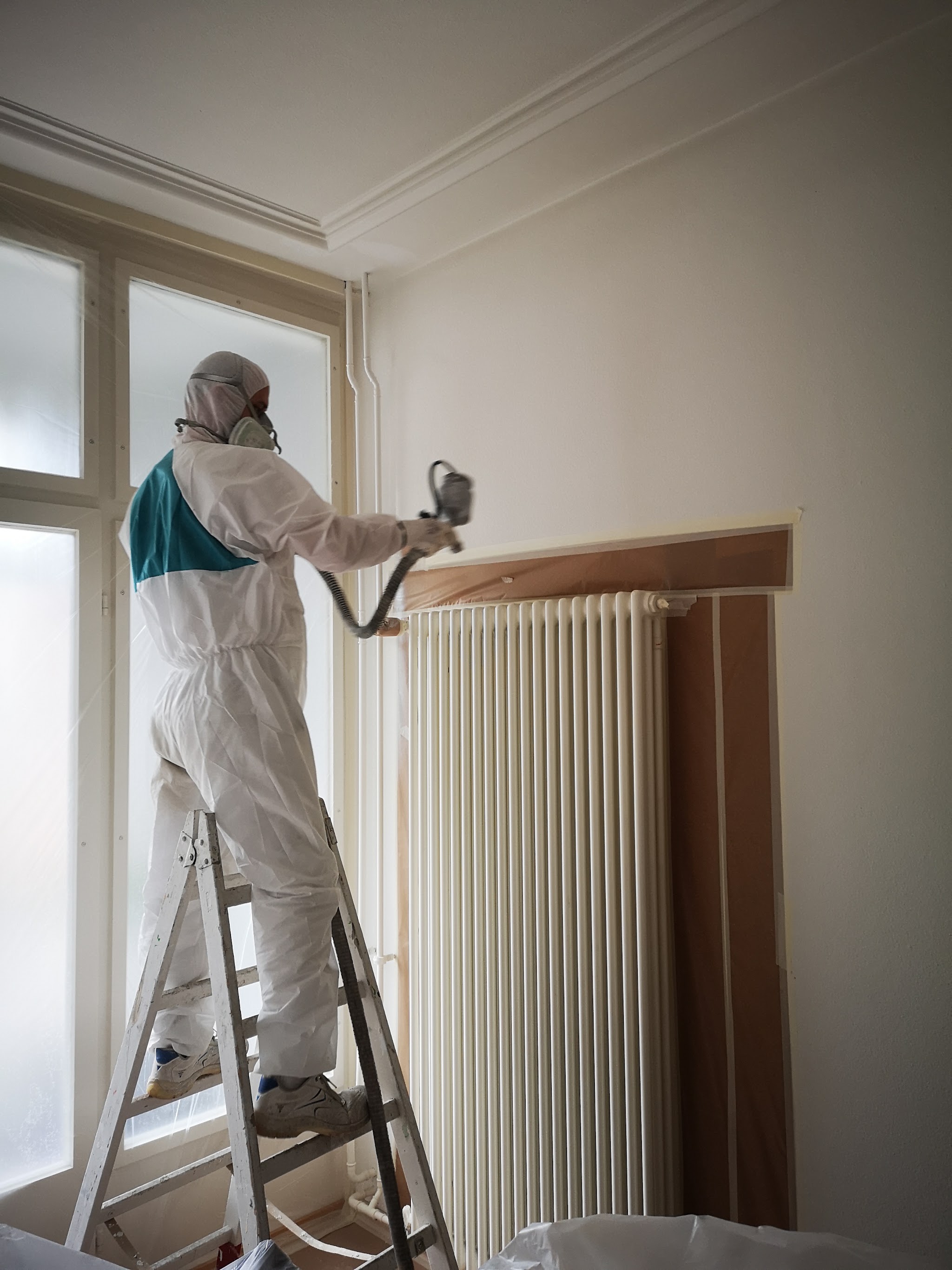 Maler spritzt einen Fensterrahmen und einen Heizkörper in einem Innenraum